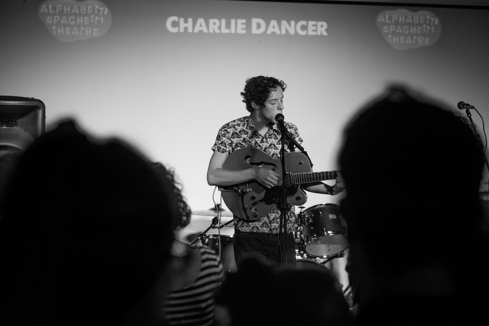 Charlie Dancer on stage in black and white, name on the screen behind